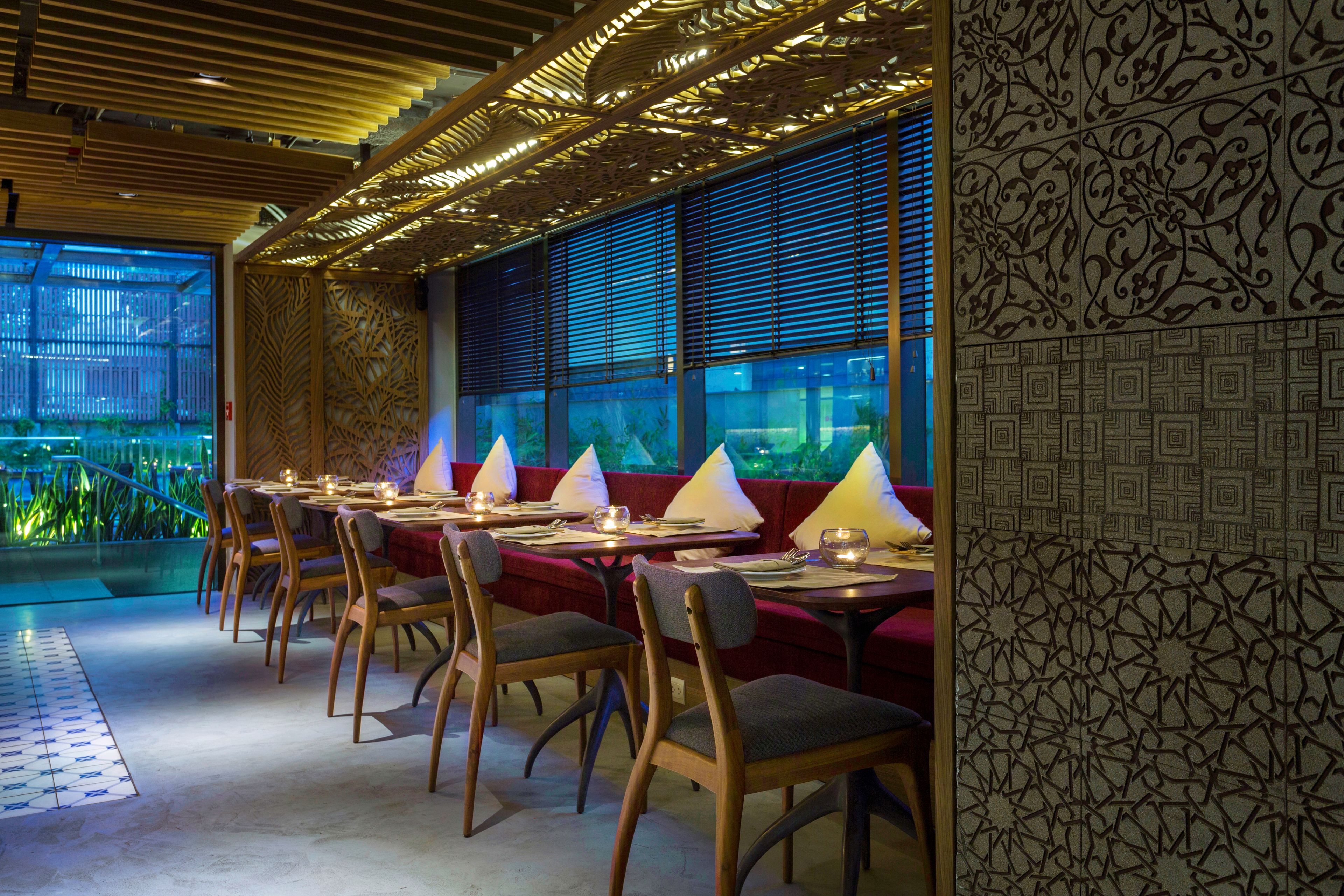 Un ristorante con sedie e tavoli in legno, una parete decorata con motivi e vista sulla vegetazione.