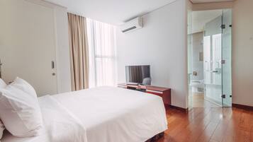 A hotel room with a bed, a TV, a desk, and a glass-enclosed shower area.