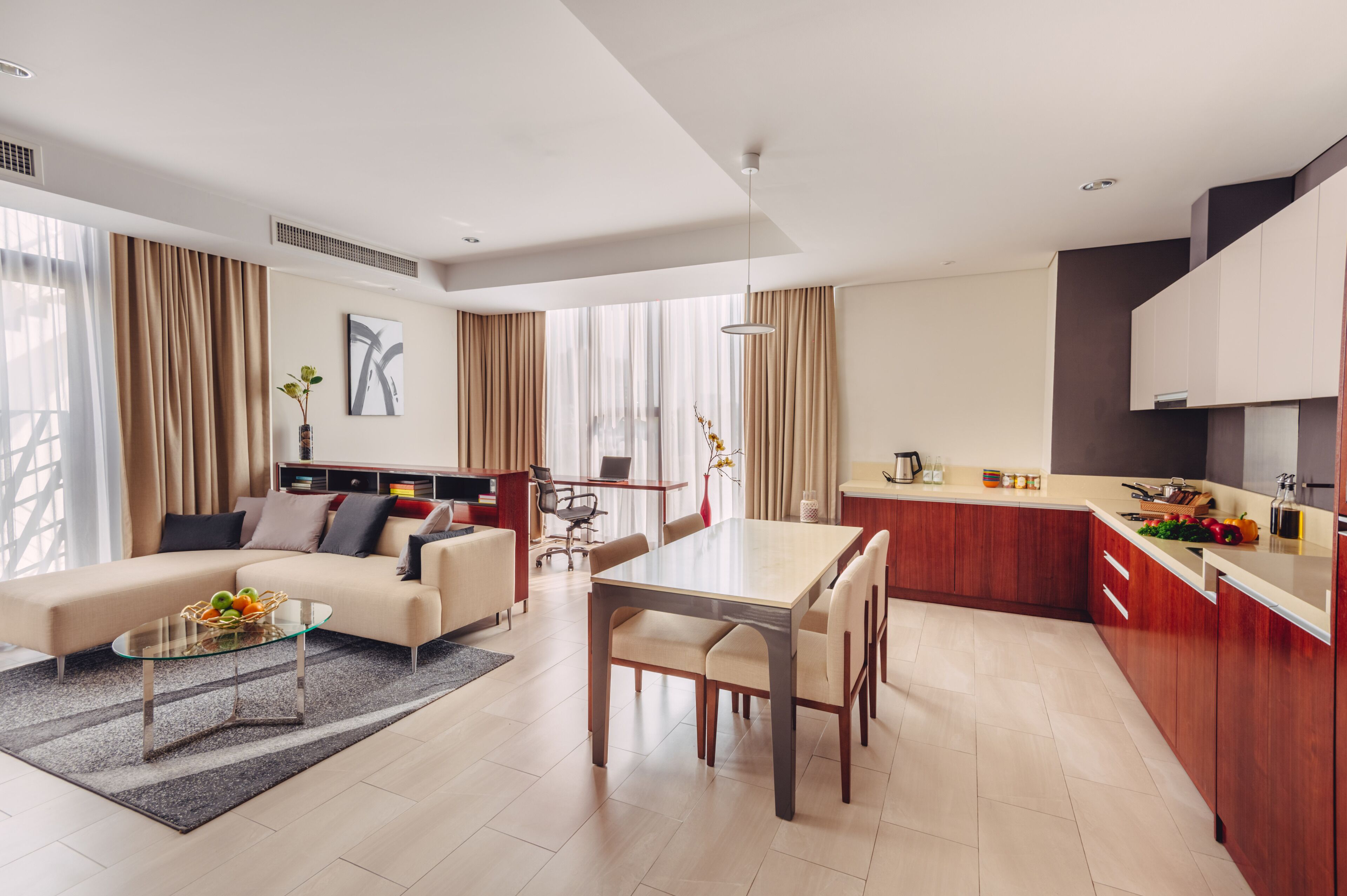 A modern living room with a sofa, coffee table, and dining area. There is a kitchen with wooden cabinets and a countertop.