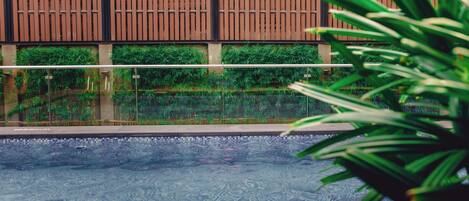 A swimming pool with a tiled edge, surrounded by a wooden fence and greenery.