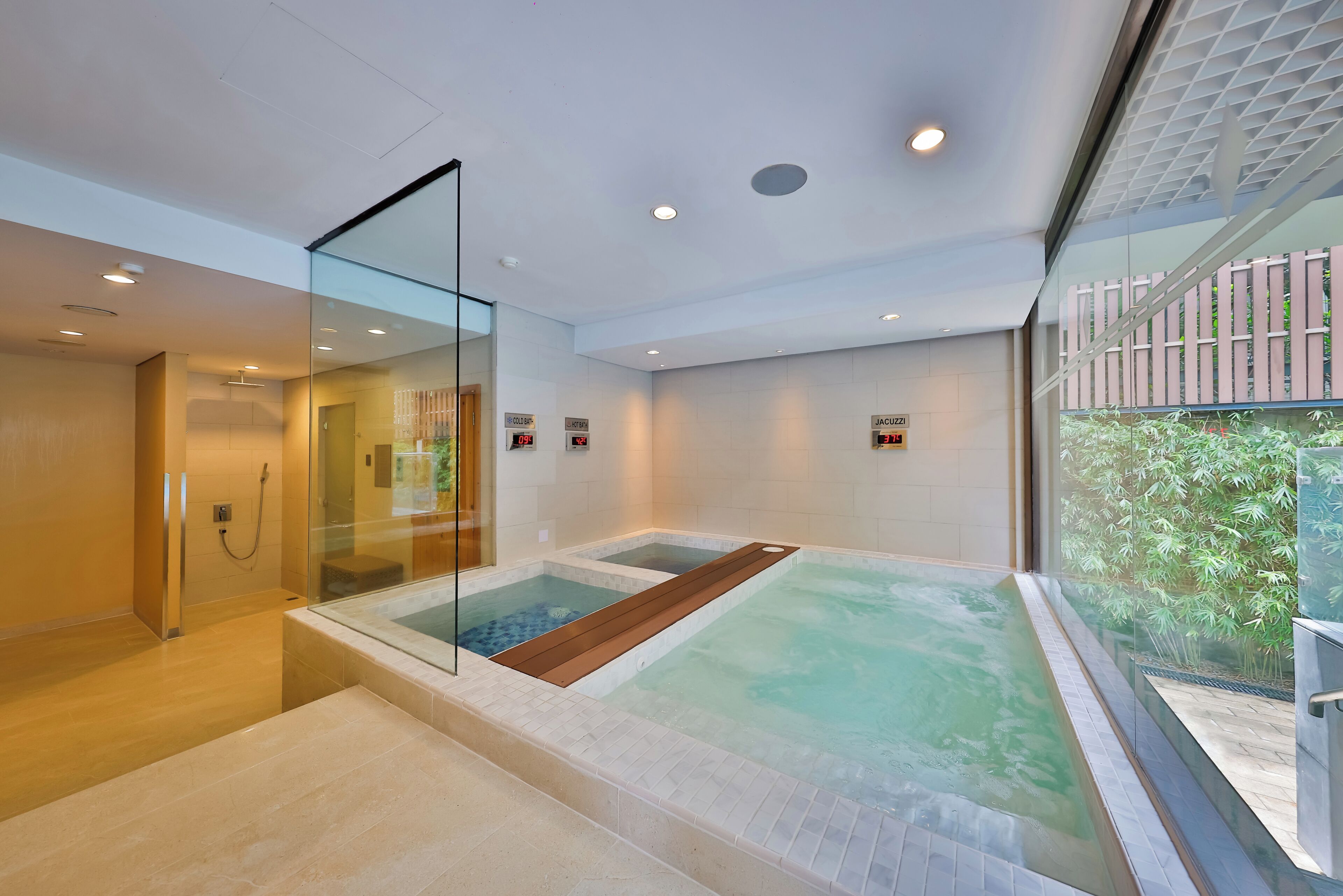 A modern spa area with a glass-enclosed hot tub, a separate cold bath, and a shower area.
