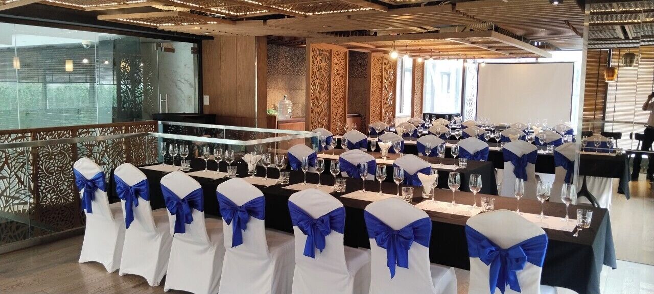 A banquet hall with tables set for a formal event, featuring white chairs with blue sashes and a long table with wine glasses and water bottles.