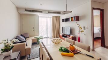 A modern hotel room with a sofa, dining table, TV, and a bookshelf.