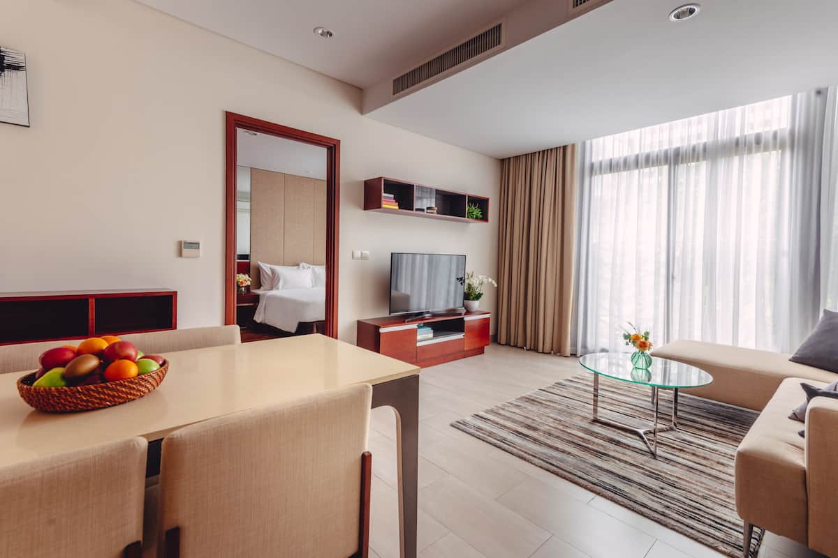 Een moderne woonkamer met een eethoek, een bank, een glazen salontafel en een tv op een houten dressoir.
