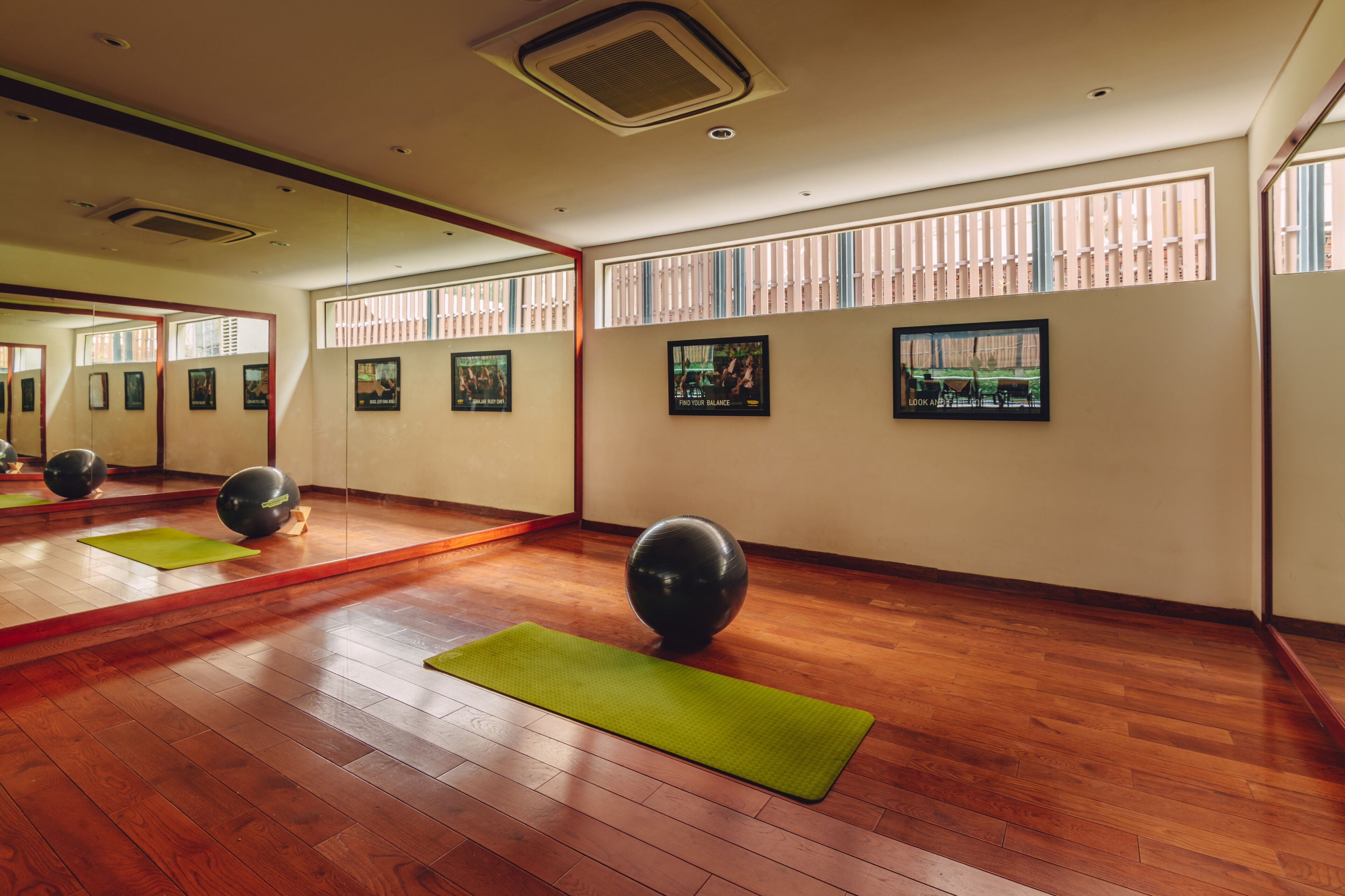 A spacious room with wooden flooring, exercise balls, and green mats.