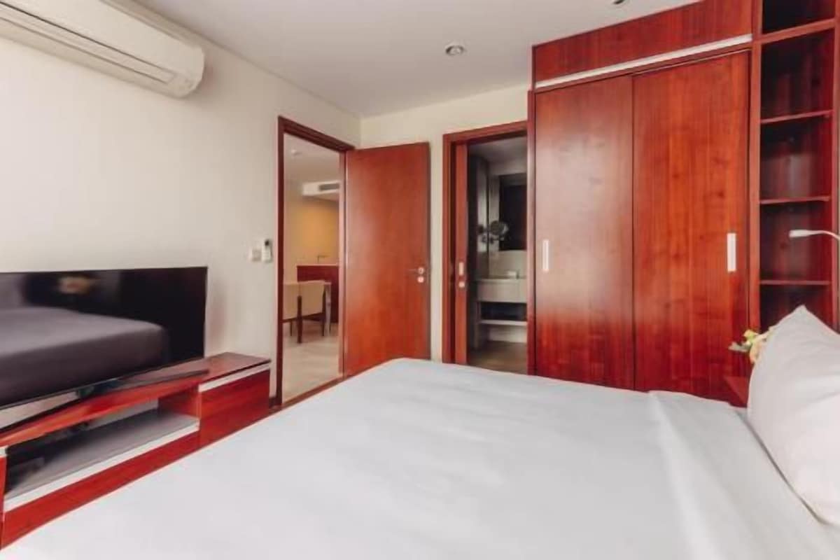 Habitación de hotel con cama, televisor, armario y baño visible a través de una puerta abierta.