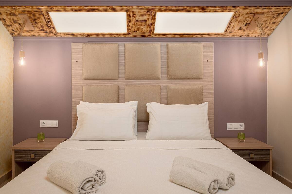 A hotel room with a large bed, two nightstands, a wooden ceiling, and a skylight.