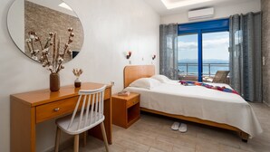 A hotel room with a bed, a desk, a chair, a large mirror, and a view of the sea. - Minos Boutique Hotel Agia Galini (Agios Vasileios)