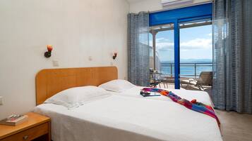 Une chambre d’hôtel comprenant un lit, une table de chevet, une table avec une chaise et un balcon avec vue sur la mer.