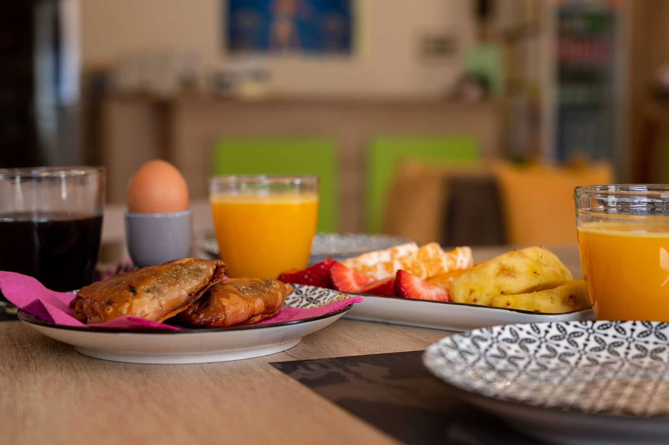 En frukostuppdukning med tallrikar fyllda med mat, inklusive bakverk och frukt, samt glas med apelsinjuice och kaffe.