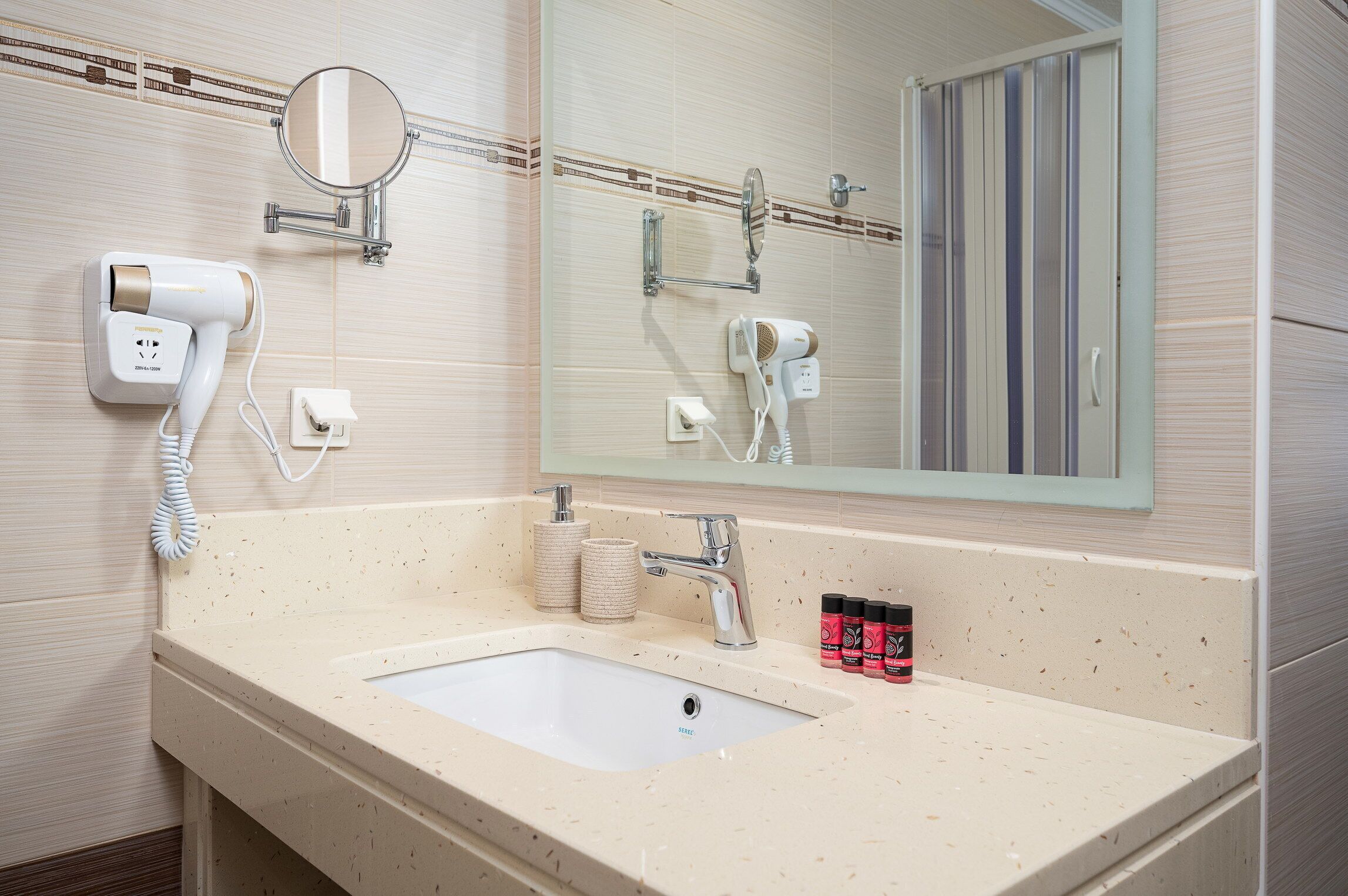 A bathroom with a sink, a mirror, a hairdryer, and a towel dispenser.