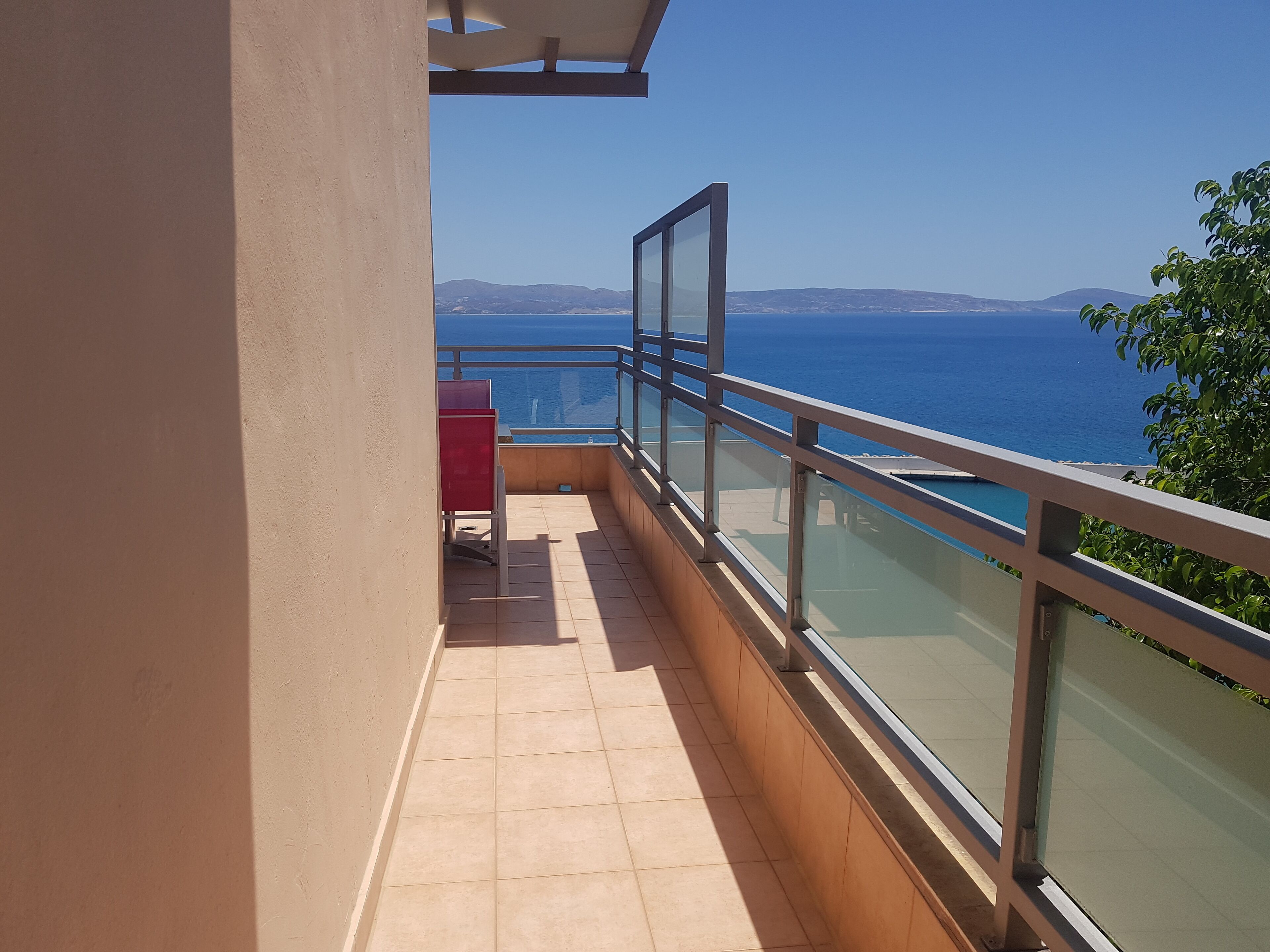 A balcony with a view of the sea, a red cabinet, and a glass railing.