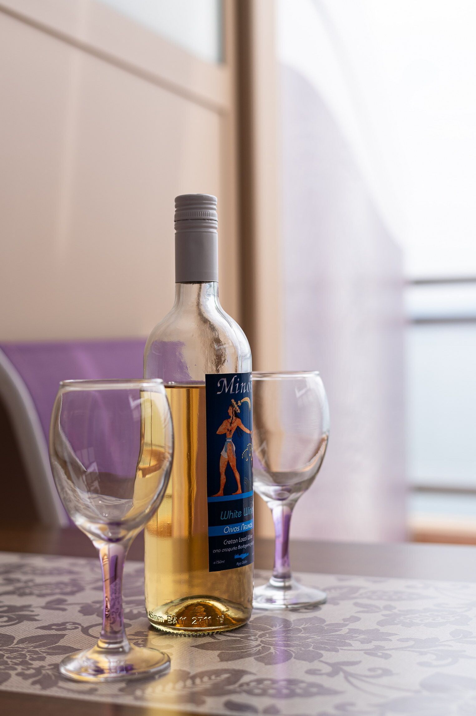 A bottle of wine and two wine glasses on a table with a floral tablecloth.