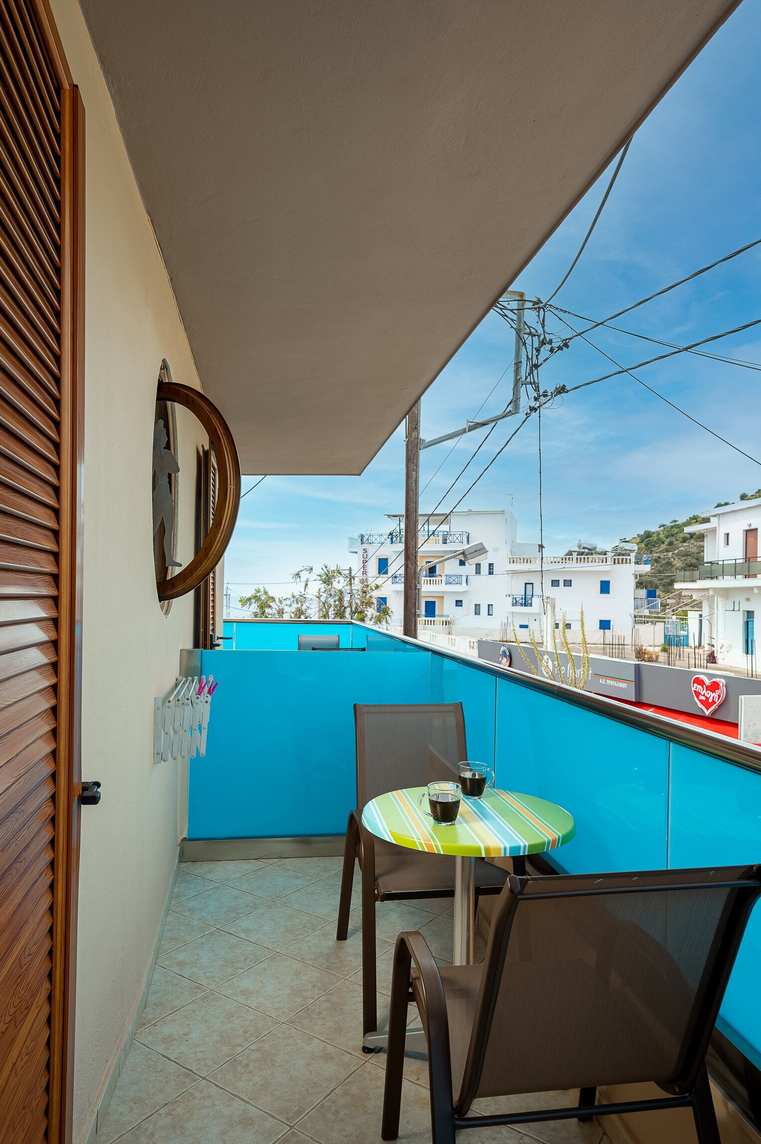 A balcony with a blue wall, a round mirror, a table with chairs, and a view of buildings in the background.