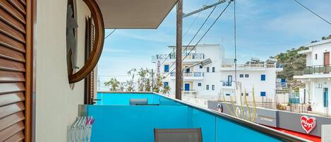 A balcony with a blue wall, a round mirror, a table with chairs, and a view of buildings in the background.