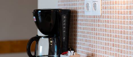 Una cocina con cafetera, lavamanos y salpicadero de azulejos.