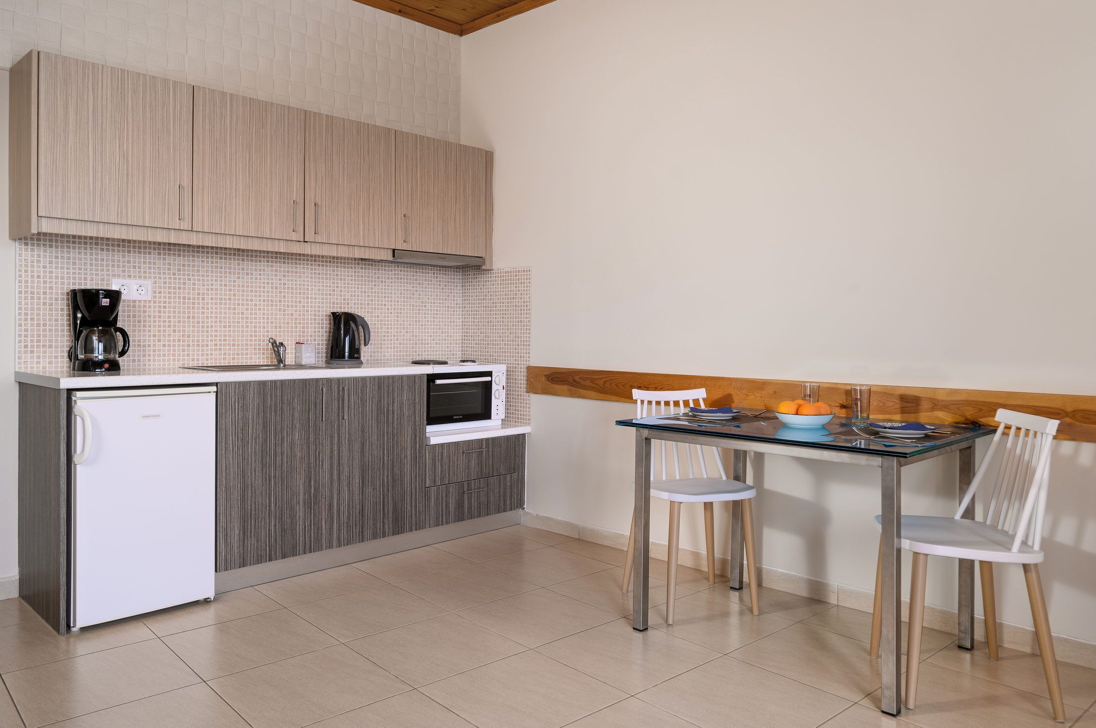 Una cocina compacta equipada con refrigerador, microondas, cafetera y una pequeña mesa de comedor con sillas.