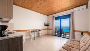 A modern kitchen with a wooden ceiling, a dining area with a table and chairs, and a sofa facing a large window with a view of the sea. - Minos Boutique Hotel Agia Galini (Agios Vasileios)
