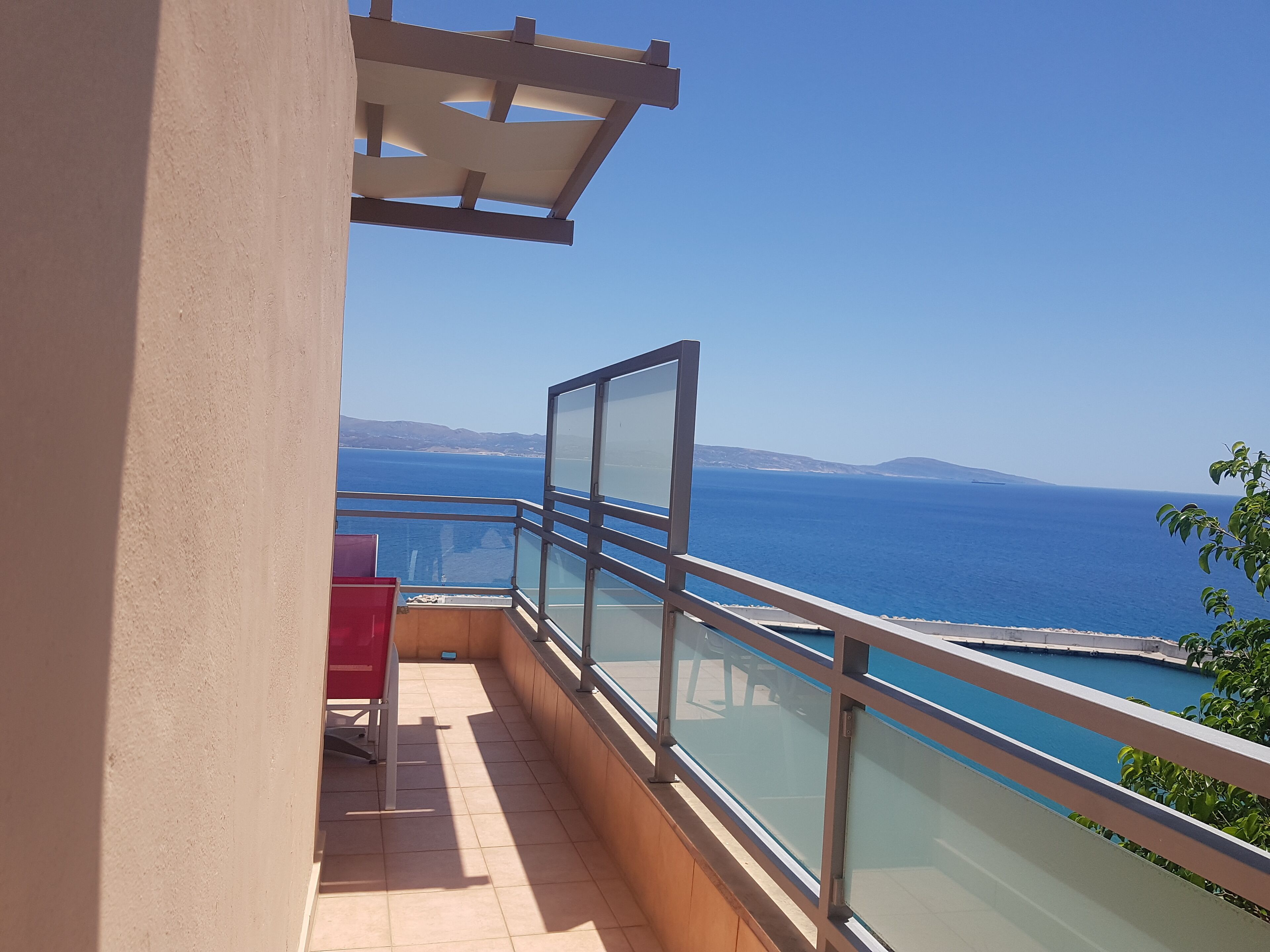 Un balcone con ringhiera in vetro che si affaccia su un corpo d'acqua e rilievi in lontananza.