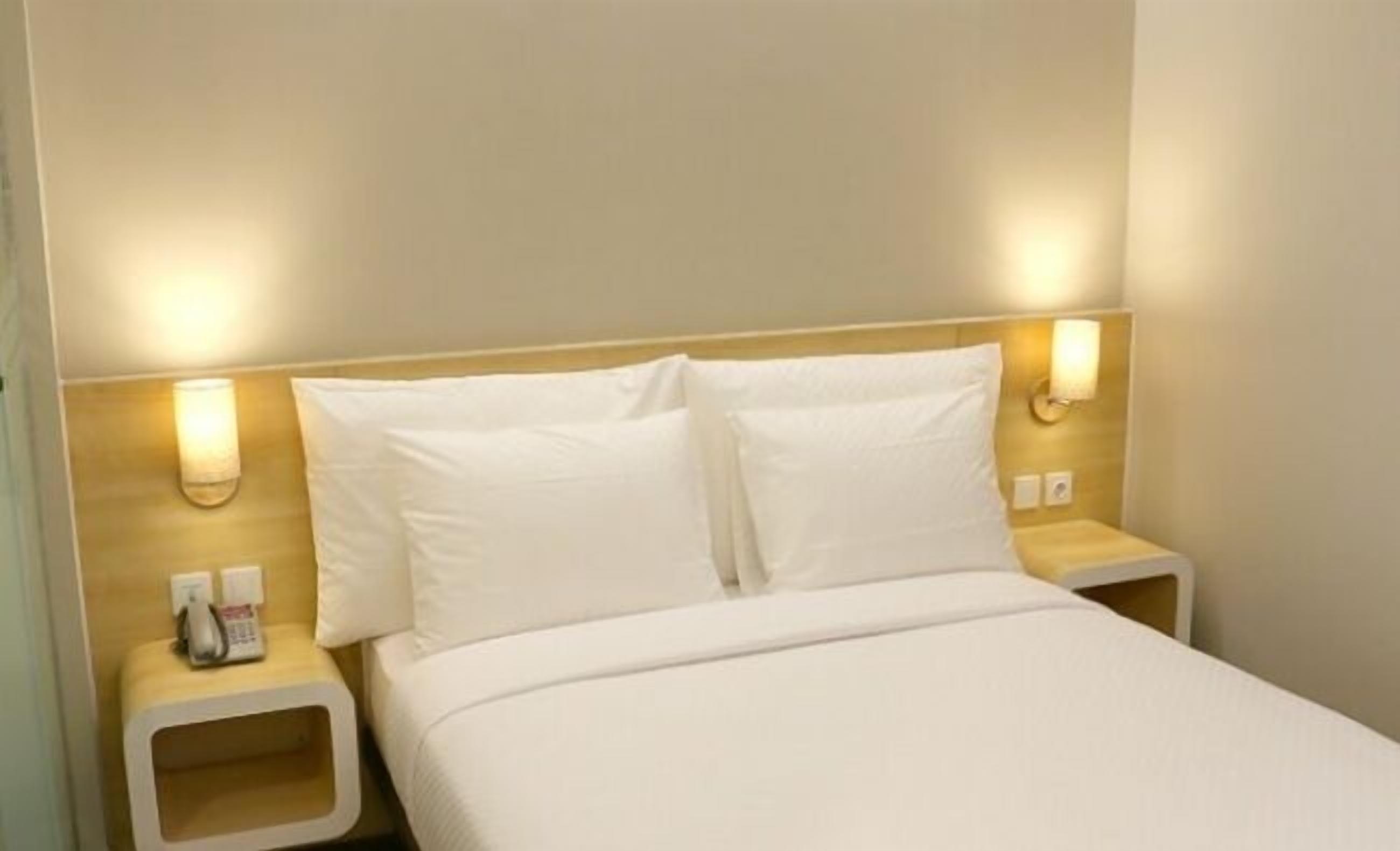 A hotel room with a bed, two bedside tables, and wall-mounted lamps.