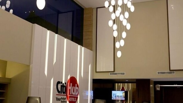 A hotel lobby with a modern chandelier, a reception desk, and a television screen. - Citihub Hotel @Kediri (Kediri)