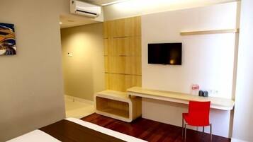 Habitación de hotel moderna con piso de madera, televisor en la pared, un escritorio pequeño y una silla roja.