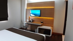 A modern hotel room with a bed, a desk with a computer, a TV mounted on the wall, and a small pet area. - Citihub Hotel @Kediri (Kediri)