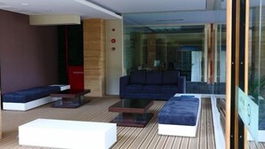 A modern living room with a sofa, ottoman, and coffee table, a red cabinet, and a glass wall. - Citihub Hotel @Kediri (Kediri)