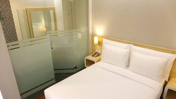 Une chambre d’hôtel comprenant un lit, une table de chevet, une lampe fixée au mur et une cabine de douche en verre.