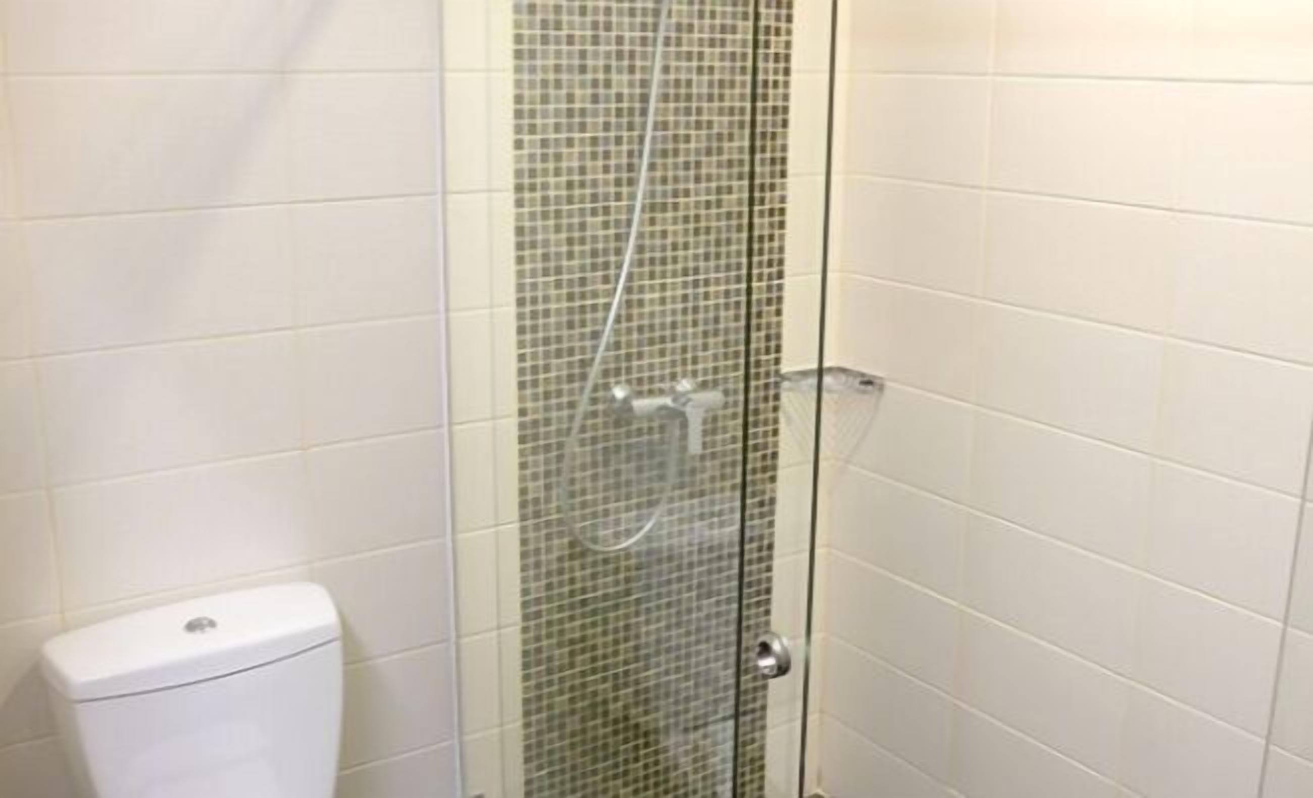 Cabina doccia con pareti in vetro, rivestimento piastrellato e un water bianco in un bagno.