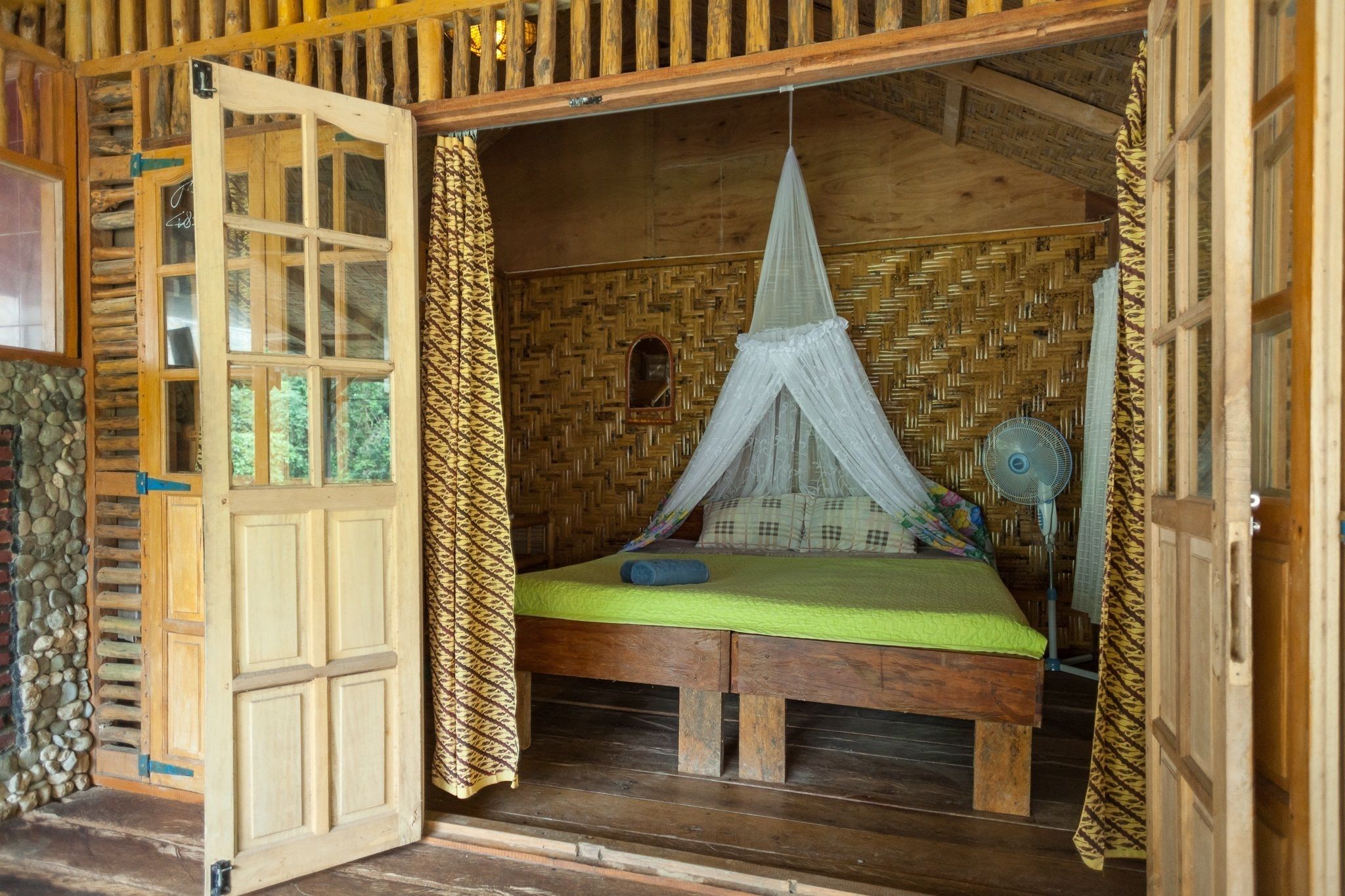 A wooden room with a bed, a fan, and a window.
