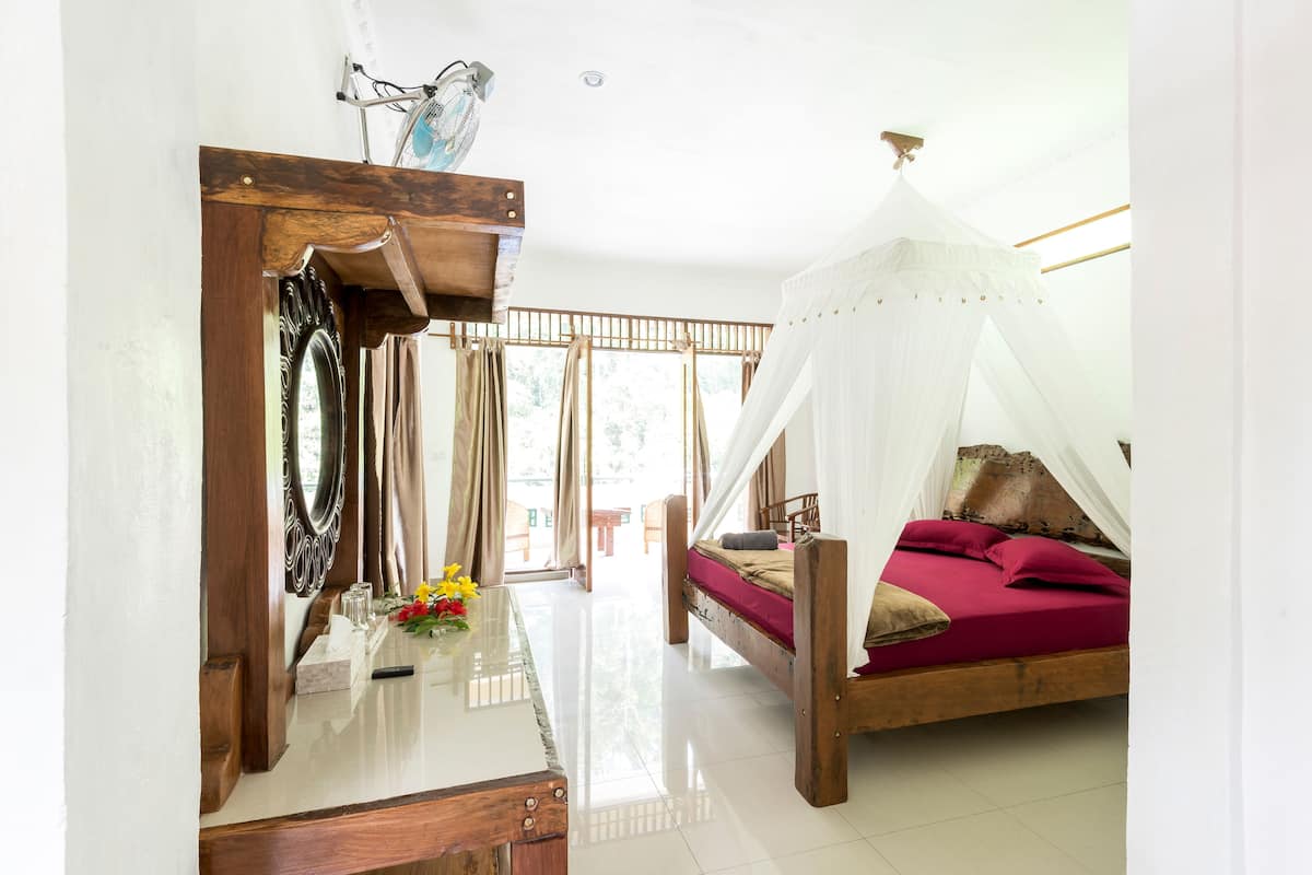 A room with a bed under a white canopy, a wooden dresser, a mirror, and a window with curtains.