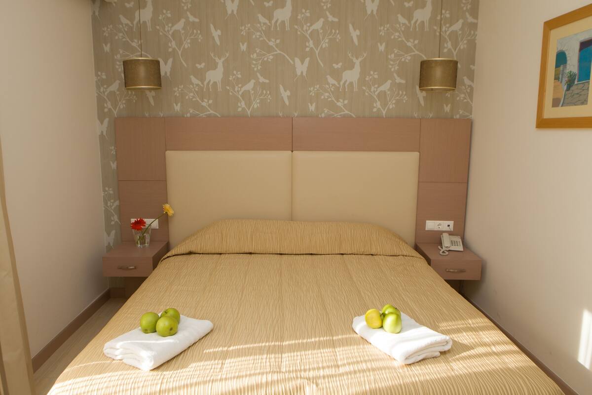 A hotel room with a large bed, two bedside tables, a nightstand, a wall-mounted telephone, and a painting on the wall.