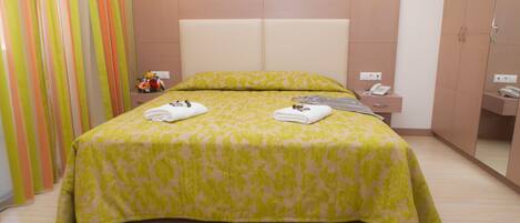 A neatly made bed with a floral bedspread, a bedside table with a lamp, and a mirror on the wall.