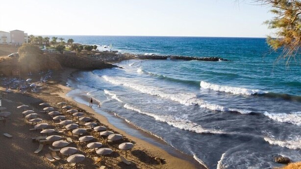 A beach with umbrellas and lounge chairs, a rocky shoreline, and a clear view of the ocean. - Panormo Beach (Mylopotamos)