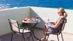A woman sitting at a table with a view of the ocean, a plate of fruit, and a glass of wine. - Panormo Beach (Mylopotamos)
