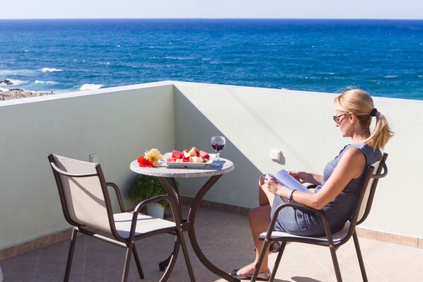 A woman sitting at a table with a view of the ocean, a plate of fruit, and a glass of wine.