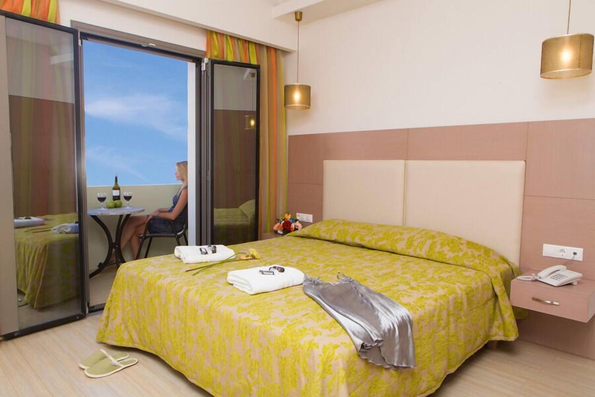 A hotel room with a bed, a bedside table, a phone, and a view through a sliding door.