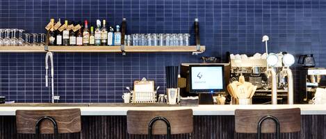 A bar area with a counter, stools, hanging lights, a coffee machine, and a tiled wall.