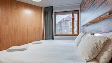 Ett hotellrum med en stor säng, väggar beklädda med träpaneler, ett fönster med utsikt över byggnader och en taklampa.