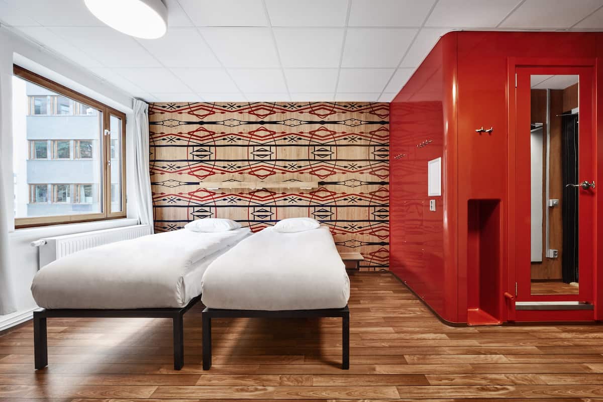 Una habitación con dos camas, una puerta roja y un papel tapiz estampado.