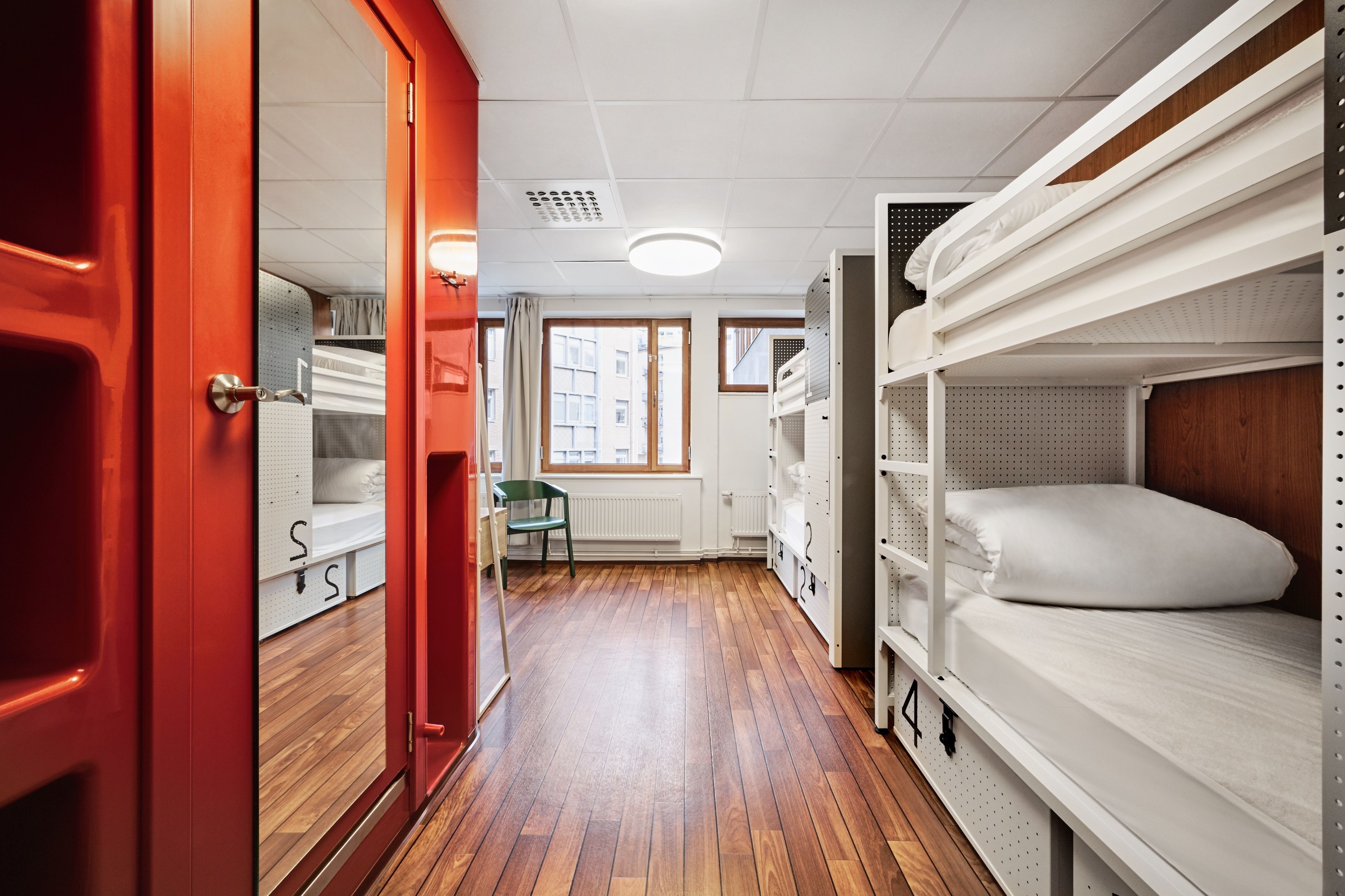 A room with bunk beds, a wooden floor, a radiator, and a window with a view of buildings.
