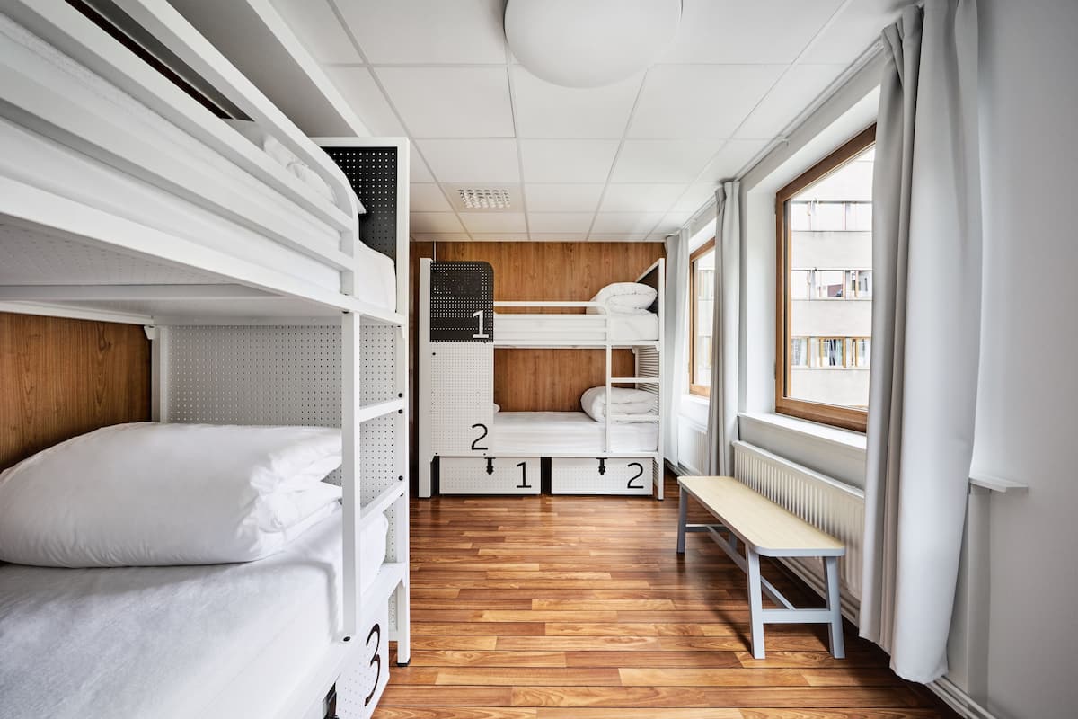 Habitación pequeña y bien iluminada con literas, suelo de madera, un banco y ventana con vistas al exterior.