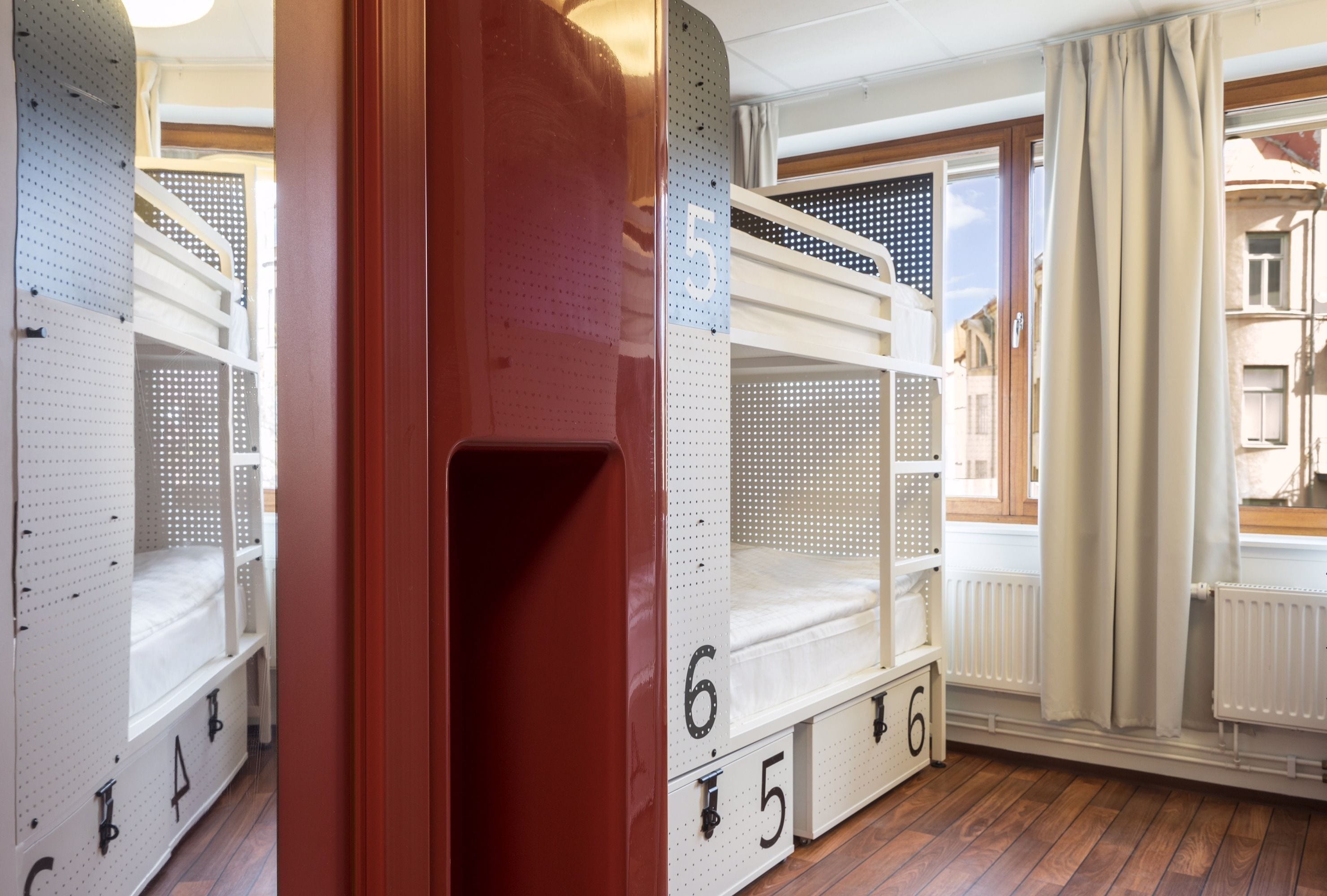 Camas literas con cajones para guardar objetos, un radiador y una ventana con cortinas.