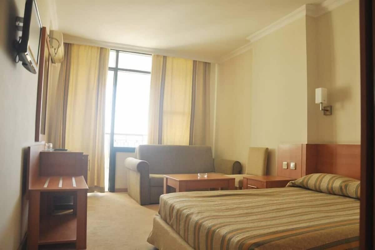 Habitación de hotel con cama, escritorio, silla, mesita pequeña y mesita de noche.