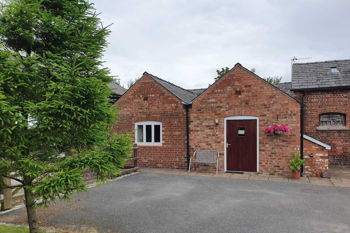 A brick building with a red door, a small window, and a bench in front.