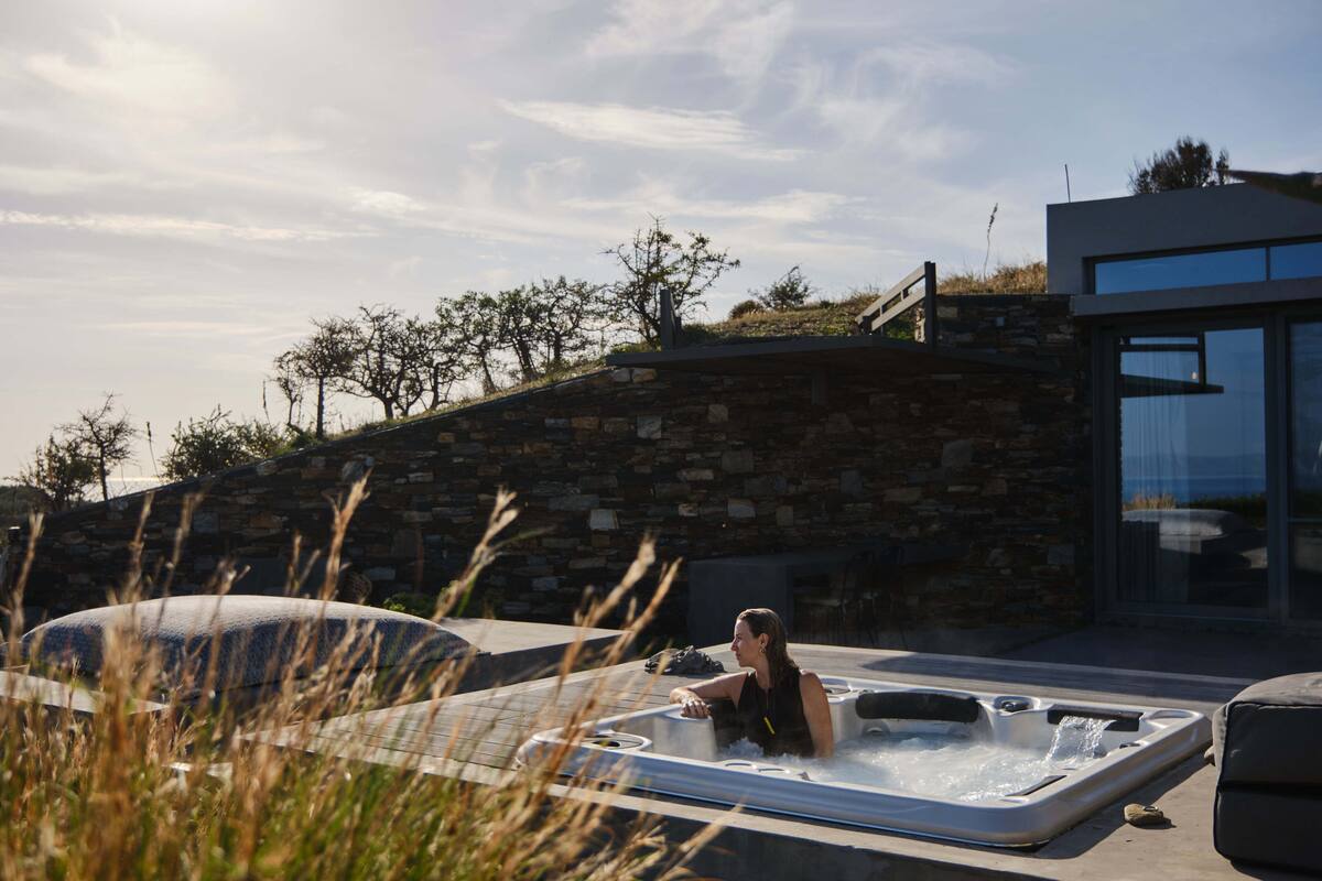 A hot tub with a stone wall and glass doors in a modern outdoor setting.