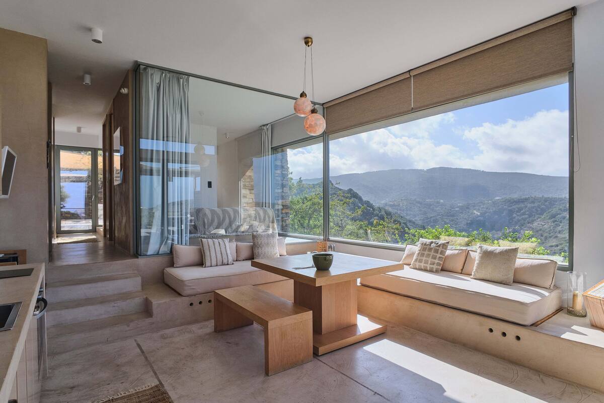 A modern living room with a large window, a wooden coffee table, and a sofa with cushions.
