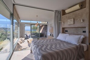 A modern bedroom with a large bed, a view of the outdoors, and a built-in air conditioning unit. - Hidden Retreats Kythera (Kithira)
