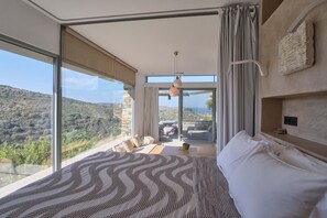 A bedroom with a large bed, a view of the countryside, a balcony with outdoor furniture, and a hanging light fixture. - Hidden Retreats Kythera (Kithira)